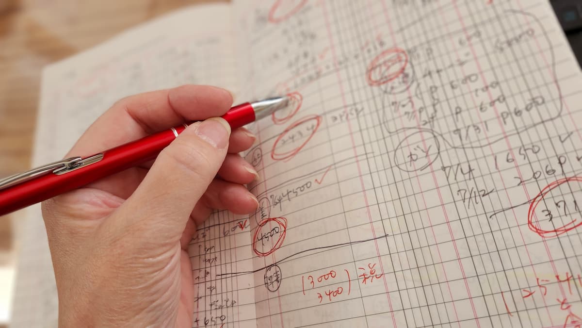 家計簿と赤いペンを持った女性の手