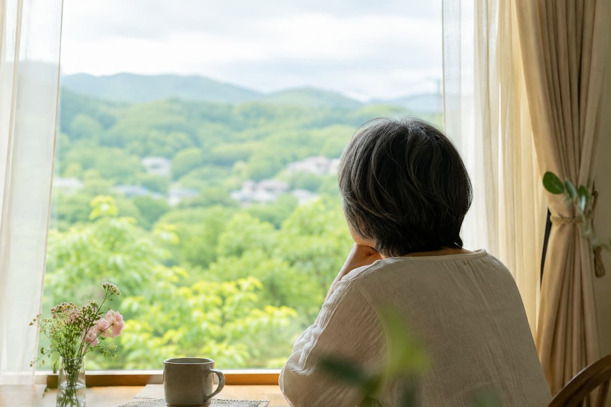 60代女性が窓の外の山々を見ている様子